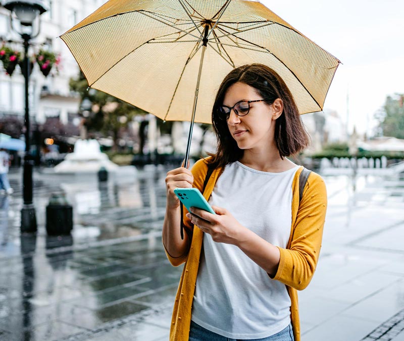 A woman with an umbrella viewing spam emails on her phone.