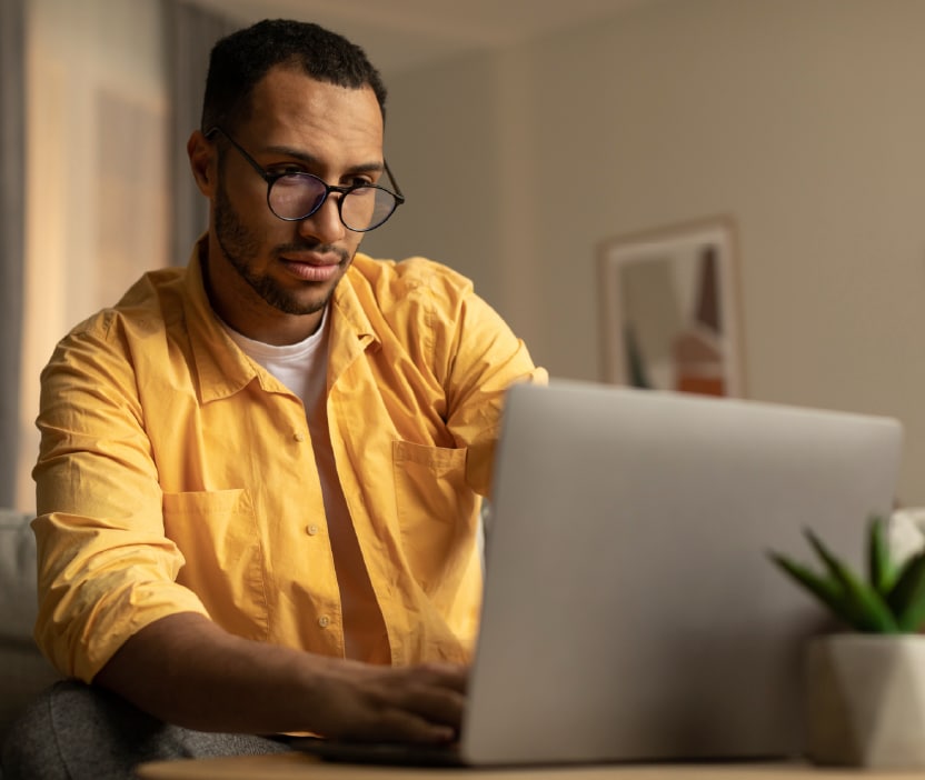 A man in a yellow shirt looking at his laptop which may be infected with spyware. 