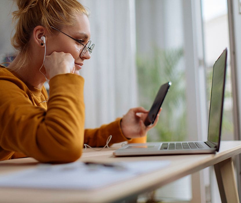 Woman sitting in front of a computer entering 2FA on her phone.