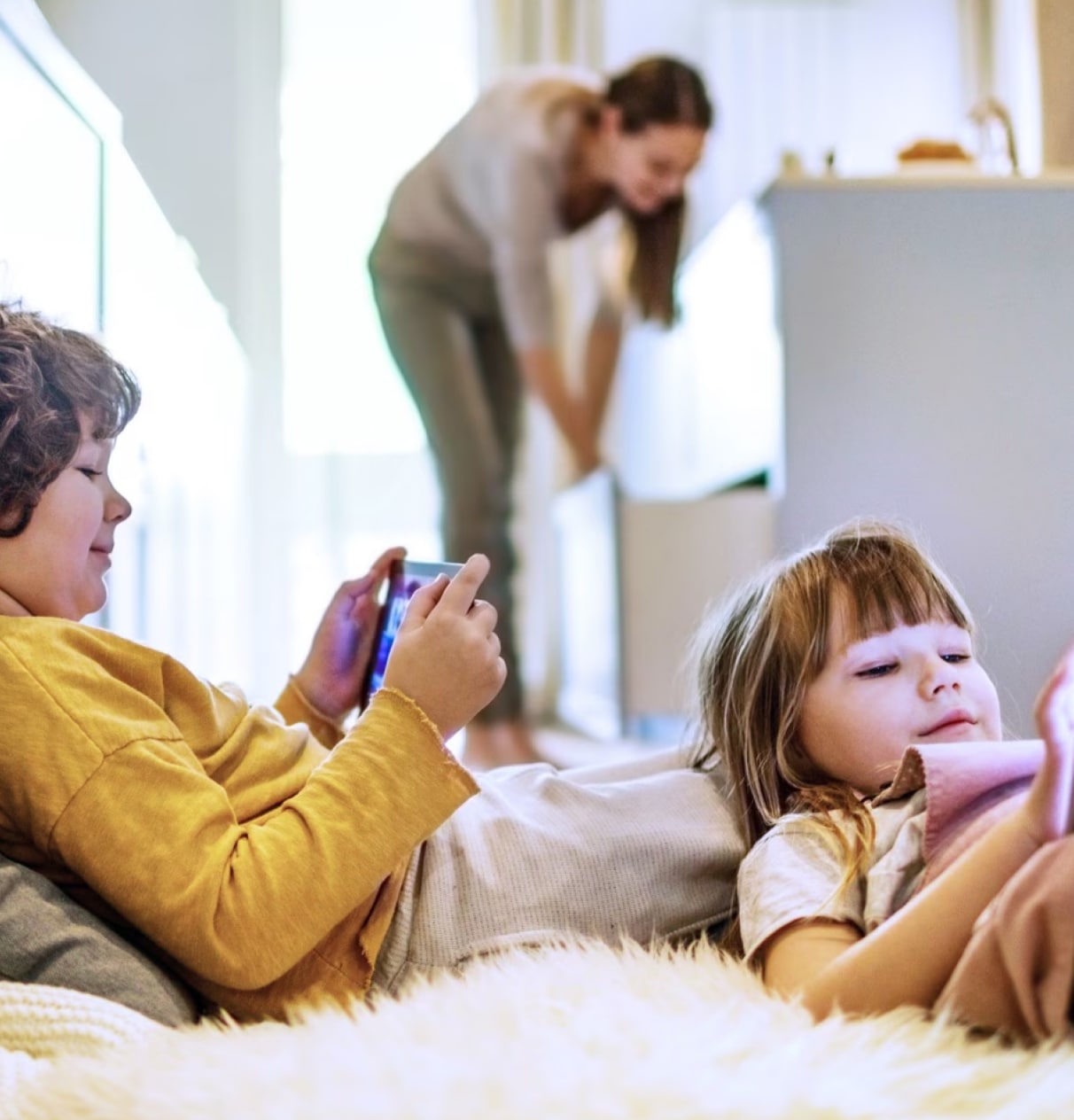 Children looking at devices while a woman is in the background