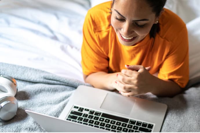 Yong woman in bed smiling looking at her LapTop.